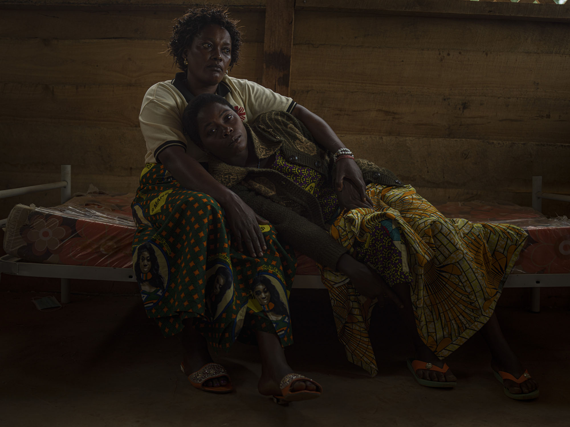 恩札樂（Nzale），30 歲，靠在歐諾琳的腿上。歐諾琳，48 歲，是負責為性侵受害者提供初步醫療並給予她們心理支持的照護員。恩札樂是在為她的七個孩子採買食物的路上遭幾個叛軍強暴，她拿不出那些逞兇者向她索要的錢財。