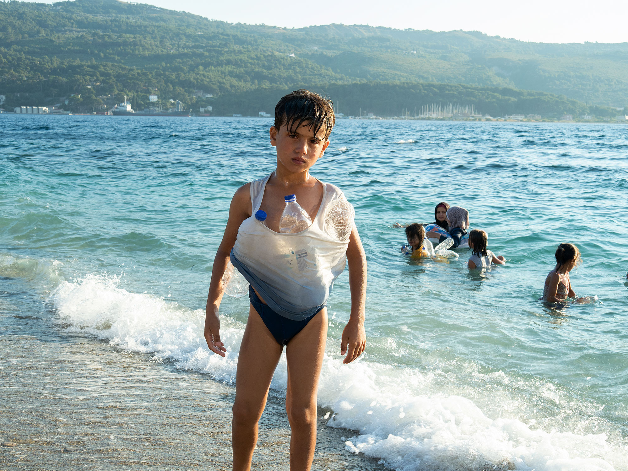 希臘，薩摩斯島，2020年7月。一名年輕的敘利亞男孩正在嘗試學習游泳，從海中返回營地。因新冠病毒疫情肆虐，所有尋求庇護者們都需要在晚上7點前回到營地。此政策只針對營地內的人，不包括當地居民。（攝影／Enri Canaj／Magnum Photos）