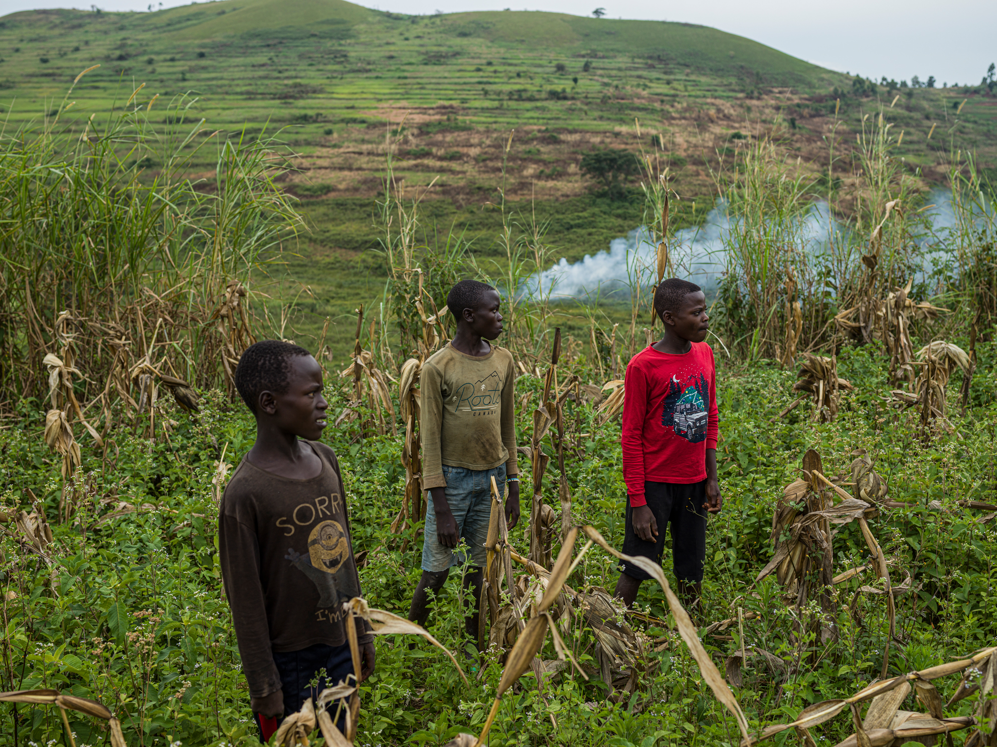 Three adolescent boys stand in a field just behind their huts in the village of Drodro.