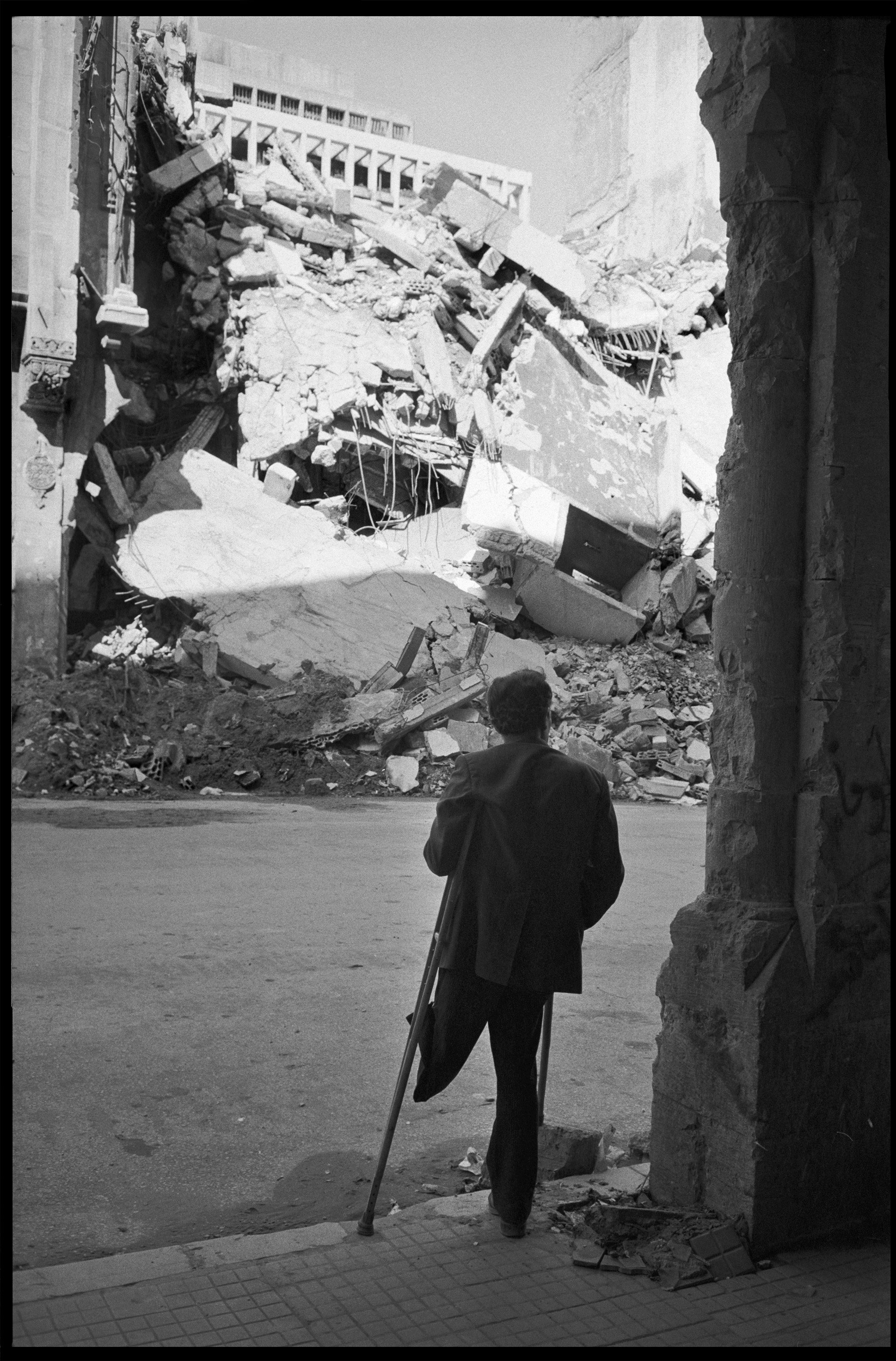 Beyrouth, Liban, 1977. Un homme amputé de la jambe gauche, vraisemblablement à cause de la guerre civile, observe un bâtiment détruit par un bombardement.