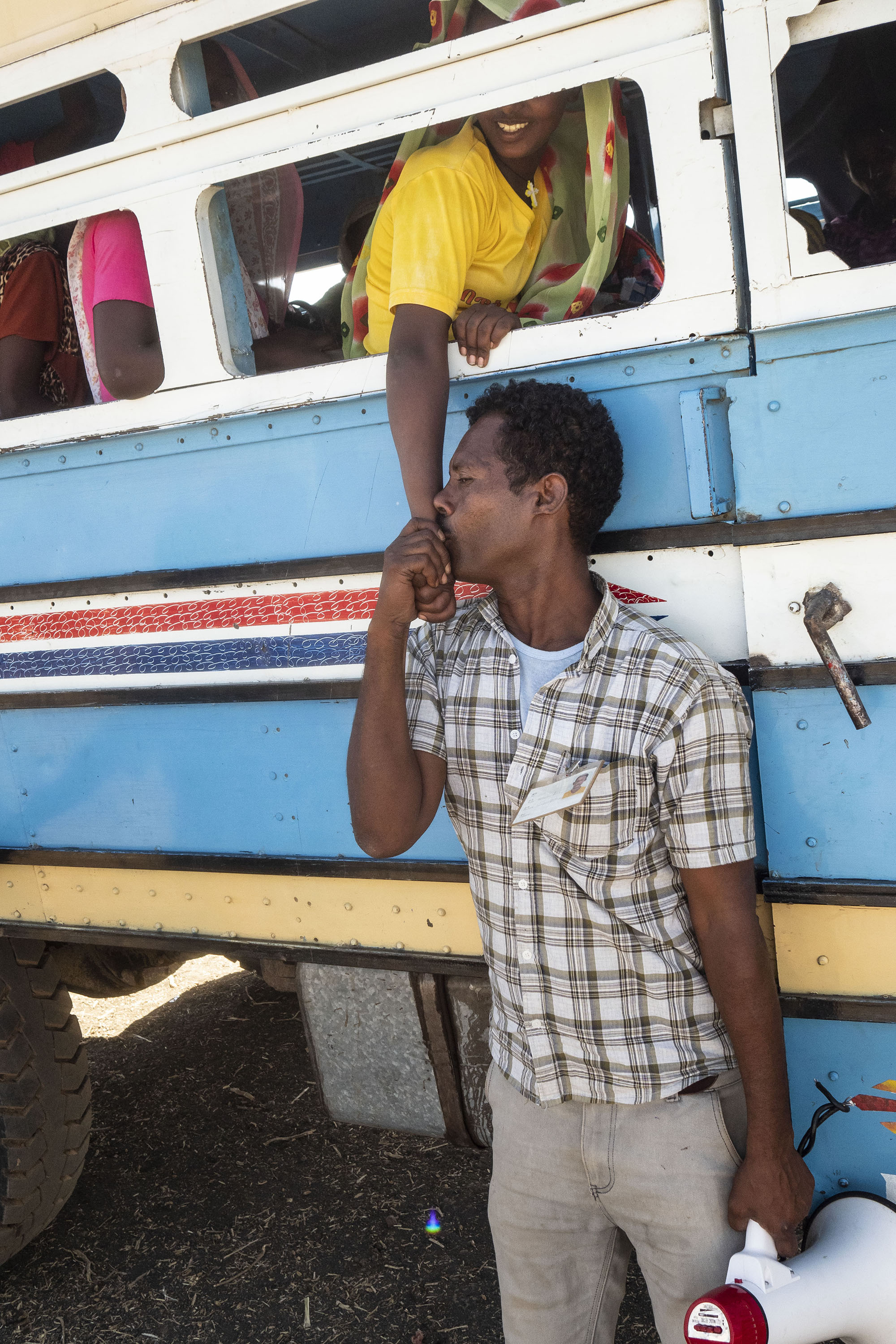 A man kisses a woman’s hand as people board buses to Um Rakuba refugee camp.